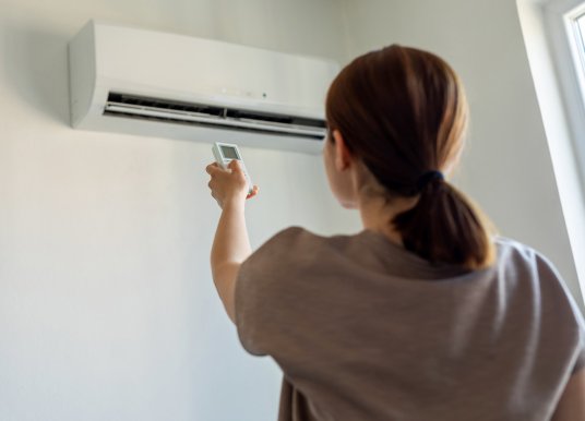 A woman switching off a wall air conditioning unit.