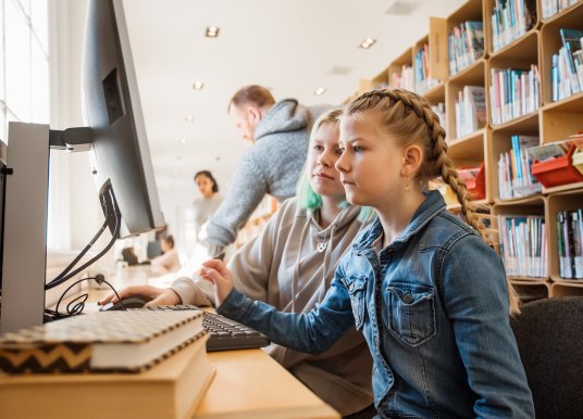 Side on view of two young girls looking at a computer screen in a public library.